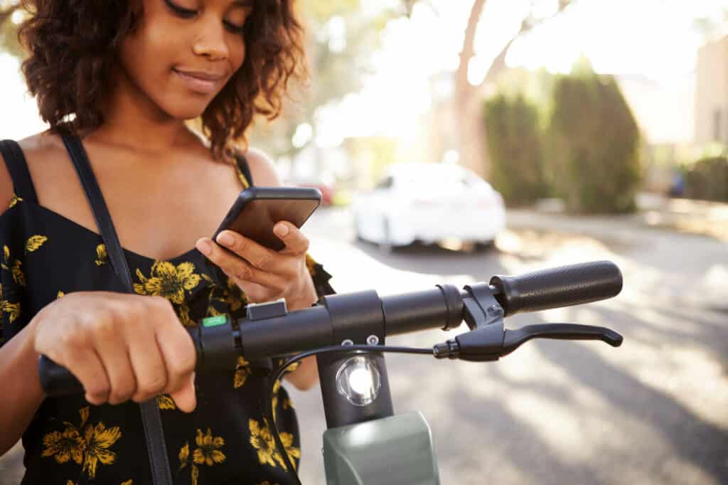 Image of woman looking at her phone while riding a scooter.